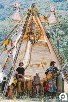 two men are playing instruments in front of a teepee