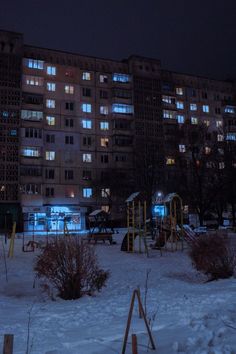 an apartment building lit up at night with snow on the ground and children's play area in front