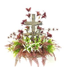 a cross and some plants on a white surface with red flowers in the foreground