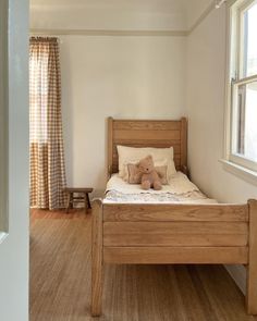 a bed with a teddy bear sitting on top of it in a bedroom next to a window