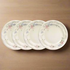 five white plates with pink and blue flowers are lined up in a row on a wooden surface