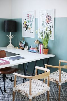 a desk with two chairs and a laptop on it in front of some pictures hanging on the wall