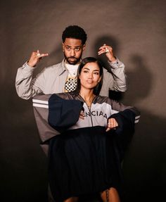 a man standing next to a woman in front of a gray wall holding an umbrella