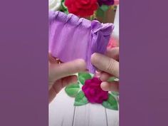 someone is making something out of paper with flowers in the background and one person's hand holding it