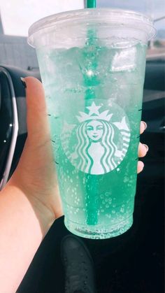 a person holding up a starbucks drink in their hand with green liquid on the cup