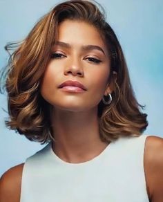 a woman with shoulder length wavy hair wearing a white top and earrings, looking off to the side