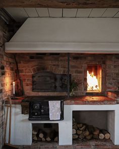 an old brick oven with logs in front of it and a lit candle on the wall