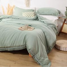 a bed with green comforter and pillows on it in a room next to a table