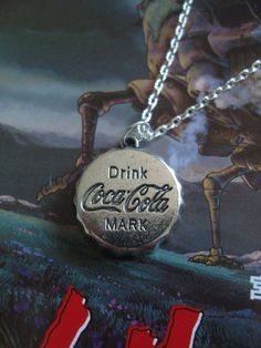 a coca cola bottle cap necklace with the word drink coke mark on it's front