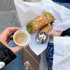 a person holding a cup of coffee and two pastries on top of white paper