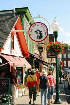 several people walking down the sidewalk in front of some shops and restaurants on a sunny day