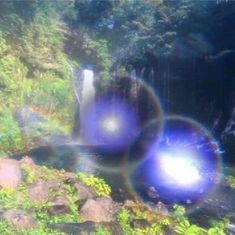 two blue balls are floating in the air near a river and waterfall with water cascading over it