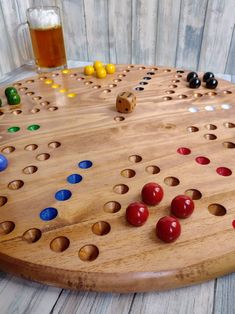 a wooden board game with several different colored pieces on it and a glass of beer in the background