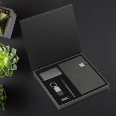 an open box with a lighter and keychain in it next to some succulents