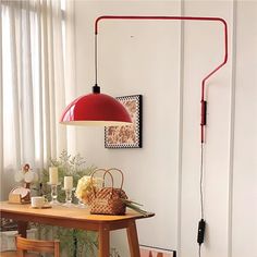 a red lamp hanging over a wooden table next to a white wall with pictures on it