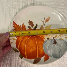 a person holding a plate with a measuring tape in front of it that is decorated with pumpkins and leaves