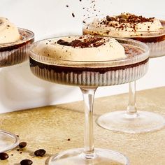 three desserts are sitting in wine glasses on a table with coffee beans scattered around them