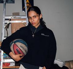 a woman holding a basketball in her hands while standing next to a stepladder