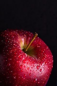 a red apple with water droplets on it's side and a glass next to it