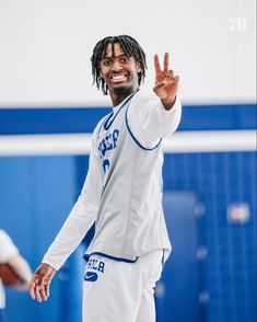 a man in white and blue uniform standing on a basketball court with his hand up