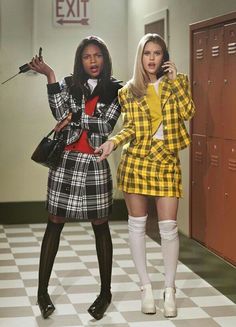 two women in plaid outfits standing next to lockers talking on their cell phones and one holding a microphone