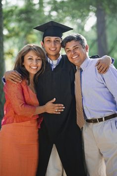 two men and a woman pose for a photo in front of trees wearing graduation gowns