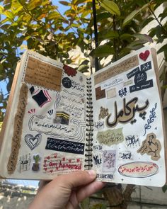 an open notebook with stickers on it in front of some trees and bushes,