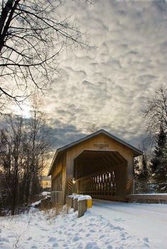 a covered bridge in the middle of winter with snow on the ground and trees around it