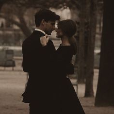 a man and woman standing next to each other in front of tree's at night