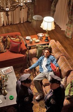 three men sitting on couches in a living room with chandelier above them