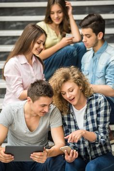 three young people sitting on the steps looking at something on a tablet computer and laughing