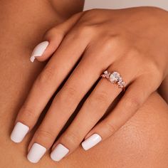 a woman's white manicured nails and ring on her left hand with an oval shaped diamond in the middle