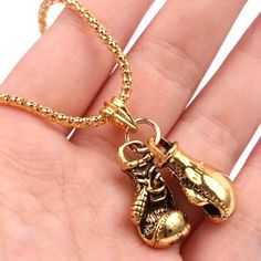 a hand holding a gold necklace with two boxing gloves hanging from it's side