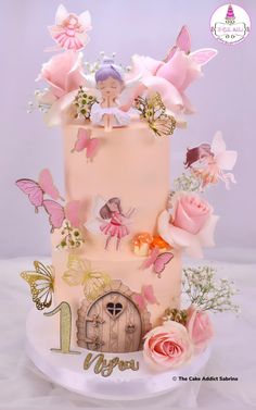 a three tiered cake decorated with pink flowers and fairy figurines