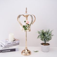 a gold crown on a stand next to a potted plant and two candlesticks