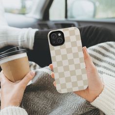 a woman holding a cup of coffee while sitting in a car with her cell phone