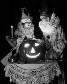 black and white photo of two people dressed as halloween characters with pumpkins on table