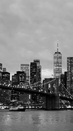 black and white photograph of the brooklyn bridge at night with city lights in the background