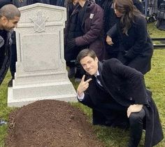 a man in a suit pointing at a grave with other people around him looking on