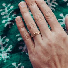 a woman's hand with a gold ring on her left hand and green floral fabric in the background