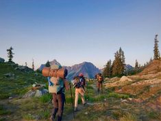 three people with backpacks walking up a trail in the mountains on a sunny day