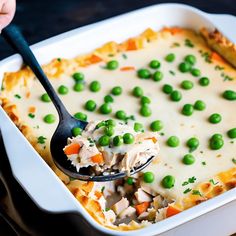 a spoon full of peas and chicken casserole in a white dish on a wooden table