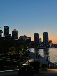 the city skyline is lit up at night as people walk along the water's edge