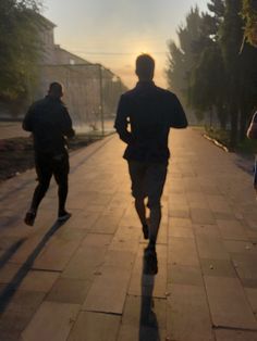 two men running down a sidewalk at sunset