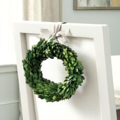 a white frame with a wreath hanging on it's side and another photo in the background