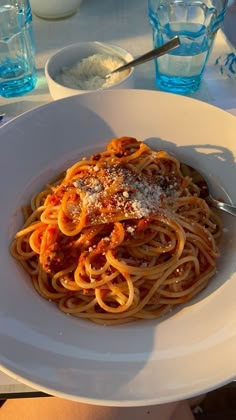 a plate of spaghetti with sauce and parmesan cheese on top, sitting on a table