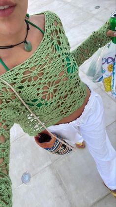 a woman wearing white pants and a green crochet top holding a cell phone