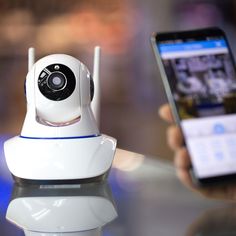 a person is holding a smart phone and a wireless security camera in front of them