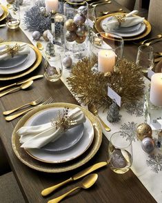 the table is set with silver and gold plates, napkins, candles and place settings