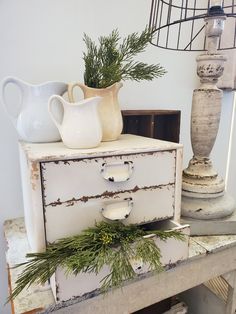 an old dresser with pine needles on top and two white vases next to it